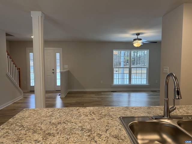 kitchen featuring sink, dark hardwood / wood-style flooring, ceiling fan, light stone countertops, and decorative columns