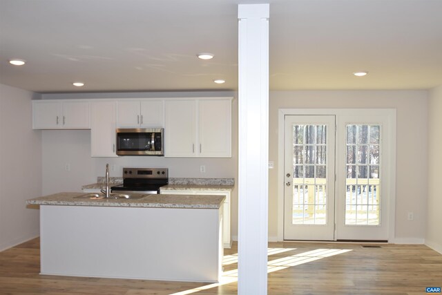 kitchen featuring white cabinetry, sink, stainless steel dishwasher, a center island with sink, and light hardwood / wood-style flooring