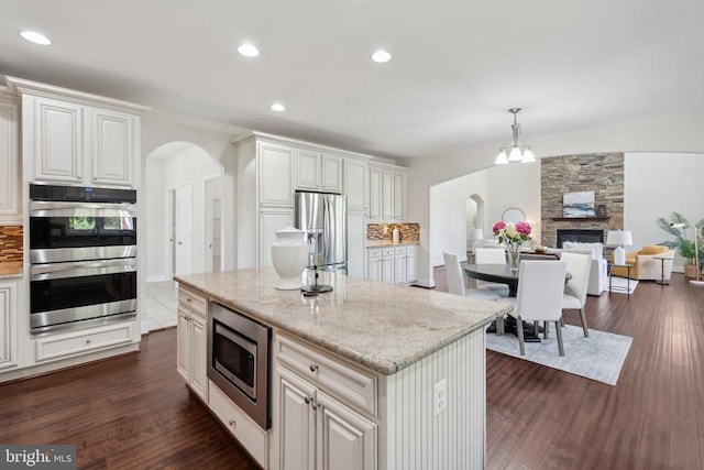 kitchen featuring arched walkways, dark wood-style flooring, light stone countertops, stainless steel appliances, and backsplash