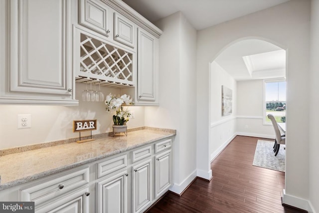 bar with a dry bar, dark wood-style floors, baseboards, and arched walkways