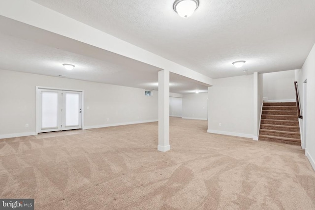 finished below grade area with light carpet, stairway, a textured ceiling, and baseboards