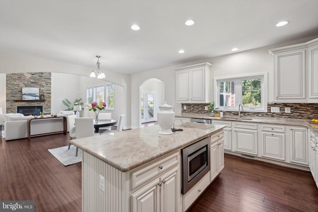 kitchen featuring dark wood-type flooring, a sink, backsplash, stainless steel microwave, and plenty of natural light