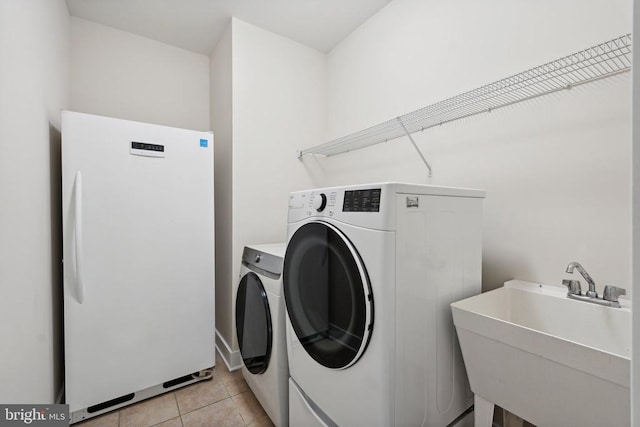 clothes washing area with laundry area, a sink, washing machine and clothes dryer, and light tile patterned floors