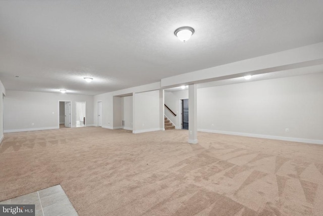 finished below grade area featuring baseboards, light colored carpet, stairway, and a textured ceiling