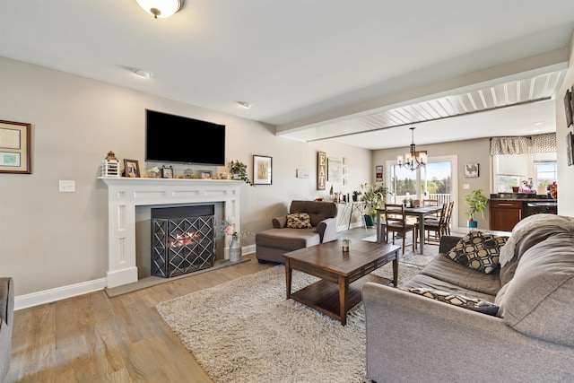 living room featuring light wood-style floors, a fireplace with flush hearth, beam ceiling, baseboards, and an inviting chandelier