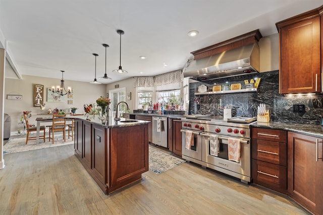 kitchen featuring backsplash, appliances with stainless steel finishes, a sink, light wood-style floors, and wall chimney exhaust hood