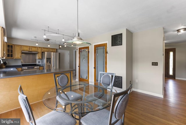 dining area with dark wood-type flooring, rail lighting, and baseboards