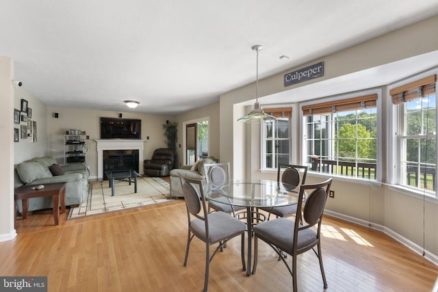 dining room with light wood-style flooring, baseboards, and a glass covered fireplace