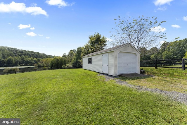 view of yard featuring driveway, a forest view, a detached garage, an outbuilding, and fence