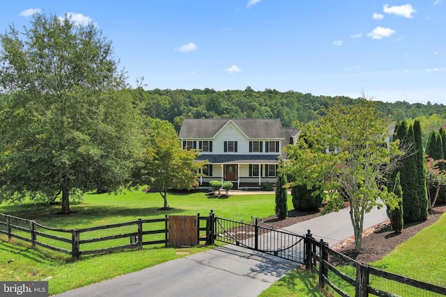 view of front facade with a fenced front yard, a yard, and a view of trees