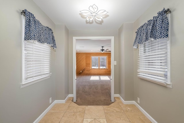 doorway featuring light carpet, wood walls, baseboards, and a ceiling fan