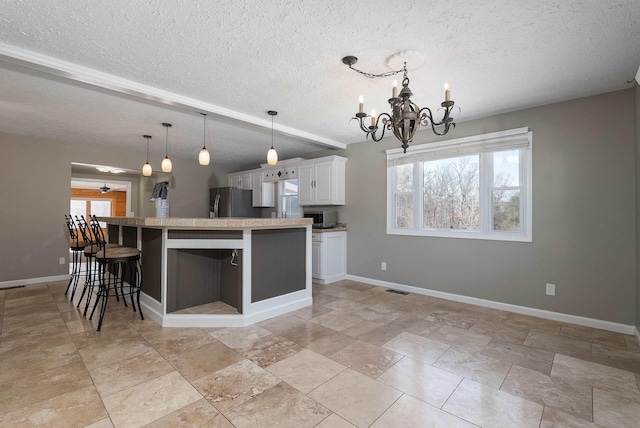 kitchen with a wealth of natural light, white cabinets, a notable chandelier, and freestanding refrigerator