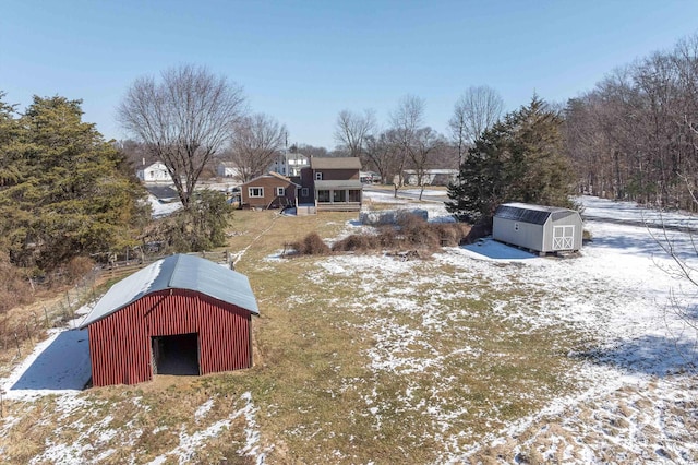 snowy yard featuring a shed, a detached garage, and an outbuilding