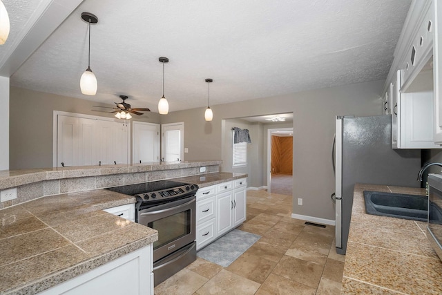 kitchen featuring tile counters, hanging light fixtures, white cabinets, a sink, and stainless steel electric range