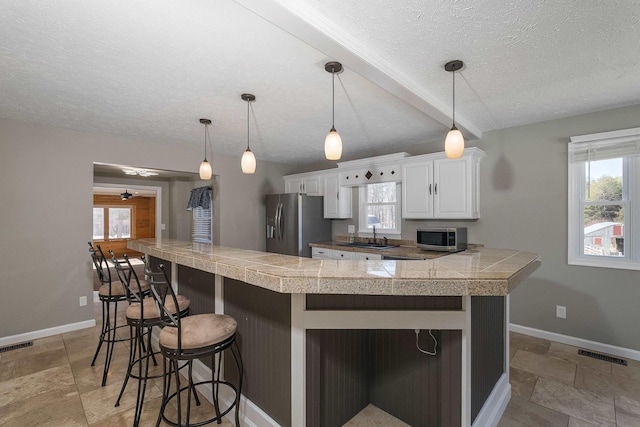 kitchen featuring tile counters, stainless steel appliances, visible vents, a kitchen breakfast bar, and baseboards