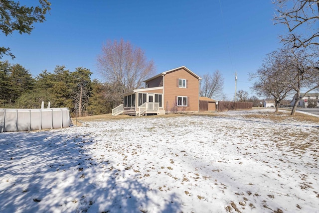 snow covered house featuring fence and a sunroom