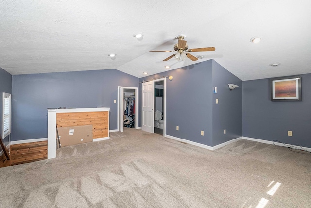 unfurnished living room featuring vaulted ceiling, ceiling fan, a barn door, and baseboards