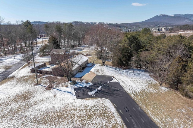 snowy aerial view featuring a wooded view and a mountain view