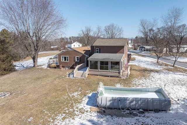 snow covered rear of property featuring a shingled roof, a sunroom, and an outdoor pool