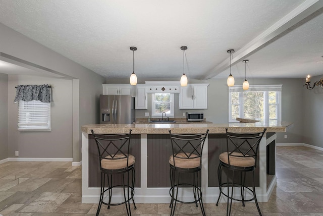 kitchen with stainless steel fridge with ice dispenser, baseboards, white cabinetry, a sink, and a kitchen breakfast bar