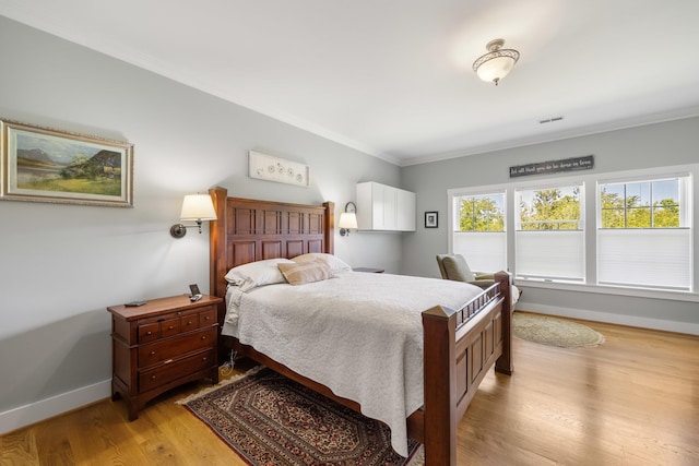 bedroom featuring light wood-style floors, visible vents, baseboards, and ornamental molding