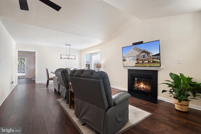 living area featuring baseboards, vaulted ceiling, ceiling fan with notable chandelier, hardwood / wood-style flooring, and a glass covered fireplace