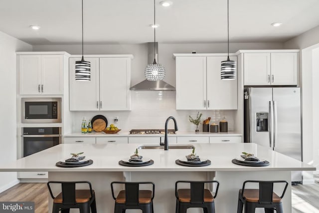 kitchen featuring wall chimney range hood, a kitchen bar, stainless steel appliances, and light countertops