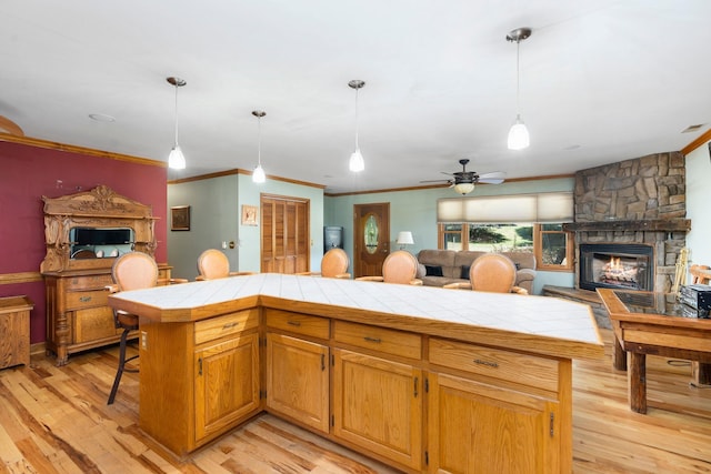 kitchen featuring light hardwood / wood-style flooring, a stone fireplace, tile counters, ornamental molding, and decorative light fixtures