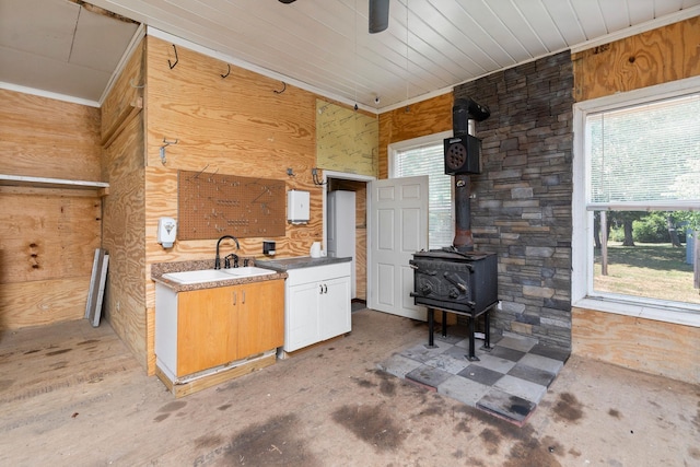 kitchen featuring a wood stove, sink, ceiling fan, and wood walls