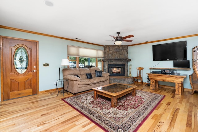 living room with crown molding, a stone fireplace, ceiling fan, and light wood-type flooring