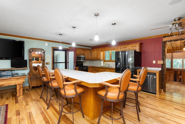 kitchen with decorative light fixtures, black appliances, ornamental molding, kitchen peninsula, and light hardwood / wood-style flooring