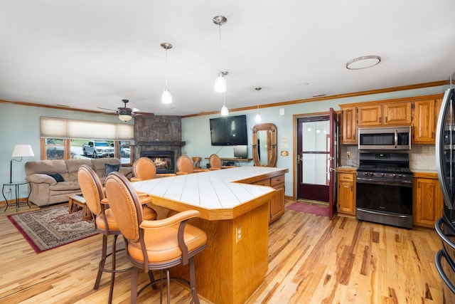 kitchen featuring appliances with stainless steel finishes, tasteful backsplash, a breakfast bar area, tile counters, and light wood-type flooring