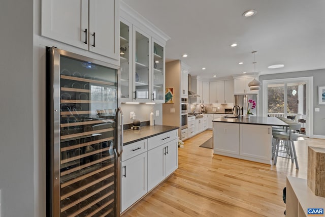 kitchen with dark countertops, beverage cooler, light wood-type flooring, stainless steel fridge, and a sink