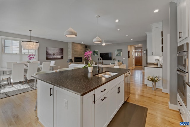 kitchen featuring a center island with sink, a sink, open floor plan, stainless steel appliances, and light wood finished floors