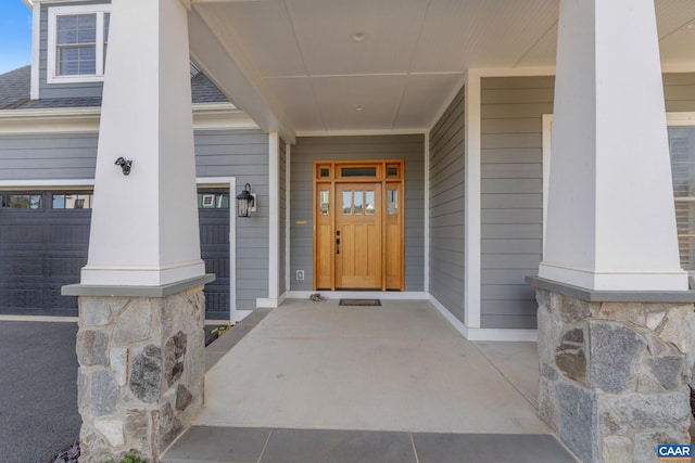 view of exterior entry featuring covered porch and a shingled roof