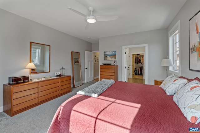 bedroom featuring a spacious closet, light colored carpet, baseboards, and ceiling fan