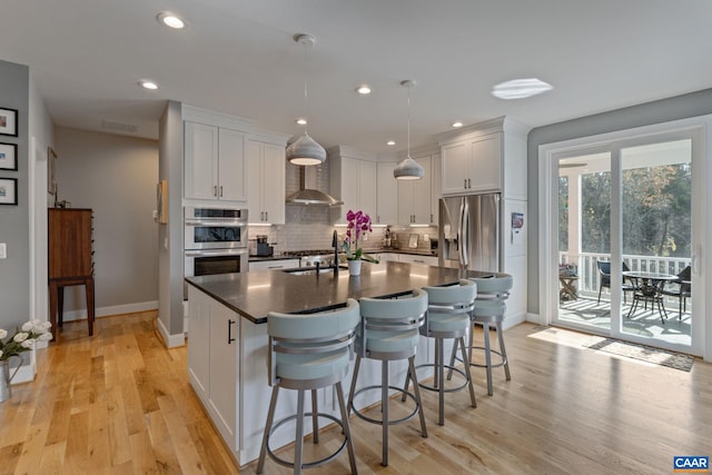 kitchen featuring a breakfast bar, stainless steel appliances, dark countertops, wall chimney range hood, and tasteful backsplash