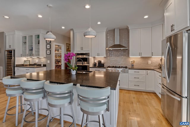 kitchen with light wood-style floors, stainless steel appliances, dark countertops, and wall chimney exhaust hood