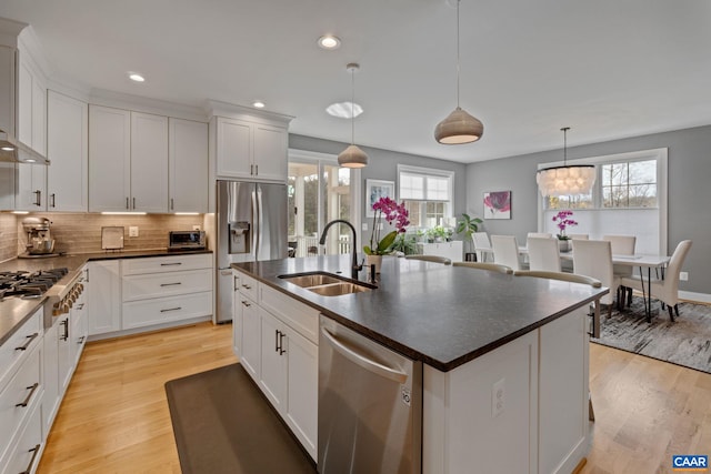 kitchen with a sink, dark countertops, appliances with stainless steel finishes, and light wood finished floors