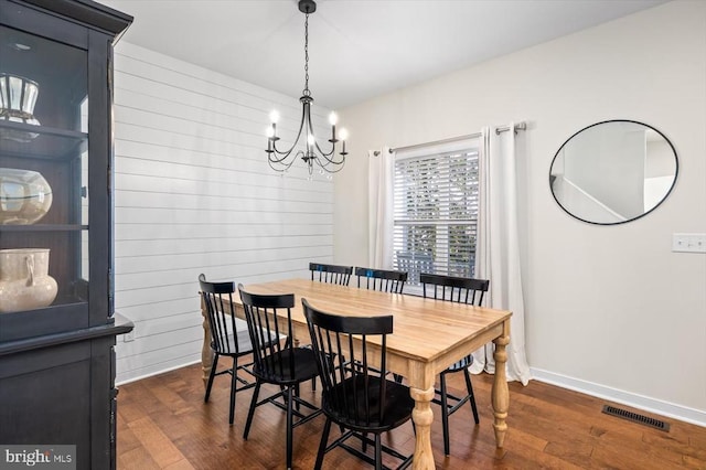 dining space featuring dark hardwood / wood-style flooring, wood walls, and a notable chandelier