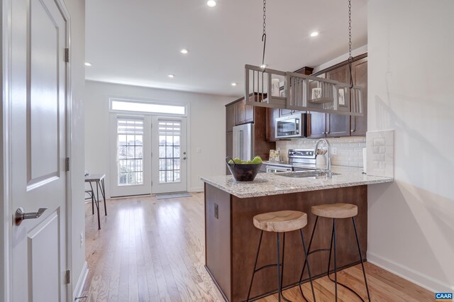 kitchen with a breakfast bar area, appliances with stainless steel finishes, kitchen peninsula, light stone countertops, and decorative backsplash