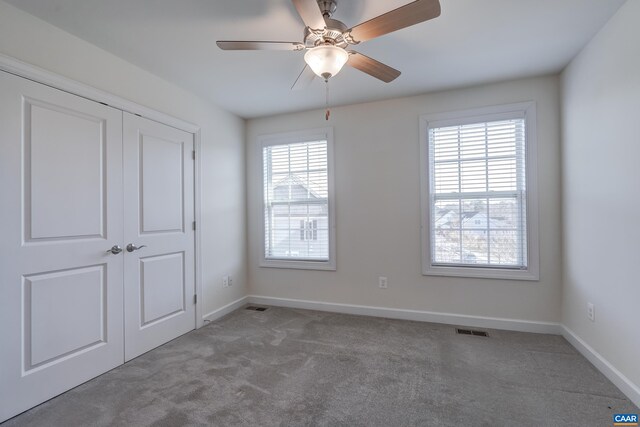 unfurnished bedroom featuring multiple windows, carpet, ceiling fan, and a closet