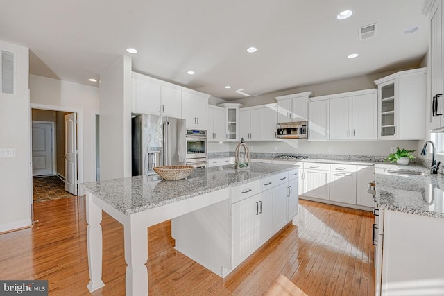 kitchen with a sink, light wood-style floors, a kitchen island with sink, stainless steel appliances, and white cabinetry