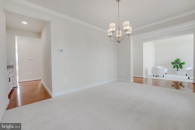 carpeted empty room with an inviting chandelier, baseboards, and ornamental molding