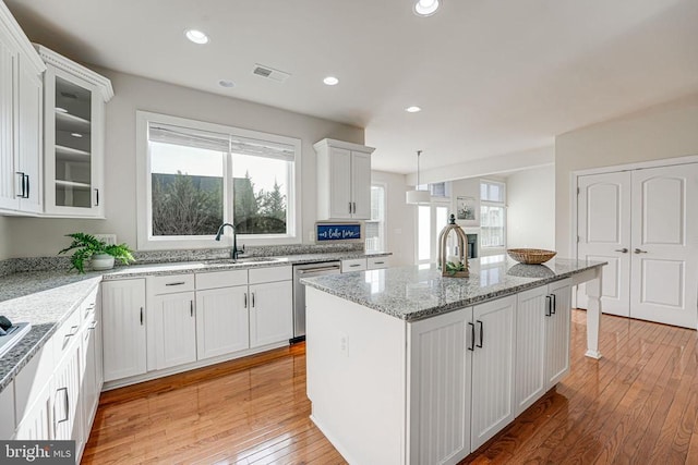 kitchen with a sink, light wood finished floors, a kitchen island with sink, white cabinetry, and stainless steel dishwasher