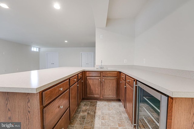 kitchen featuring brown cabinetry, light countertops, a peninsula, beverage cooler, and recessed lighting