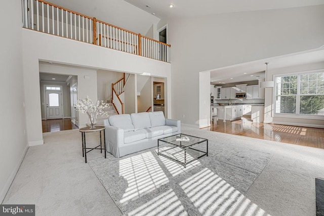 living area featuring stairway, baseboards, light carpet, and a towering ceiling