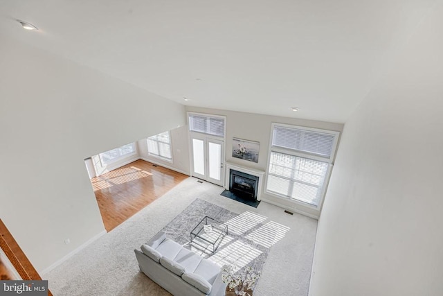 carpeted living room with a fireplace with flush hearth, baseboards, plenty of natural light, and visible vents