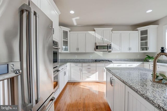 kitchen with white cabinets, light wood finished floors, stainless steel appliances, recessed lighting, and glass insert cabinets