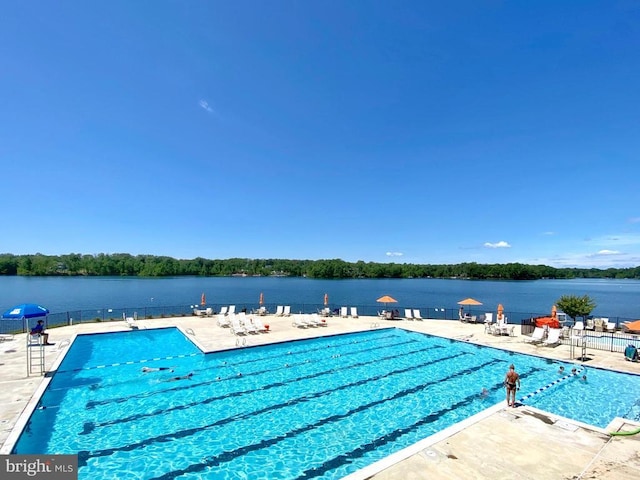 community pool featuring fence, a water view, and a patio area